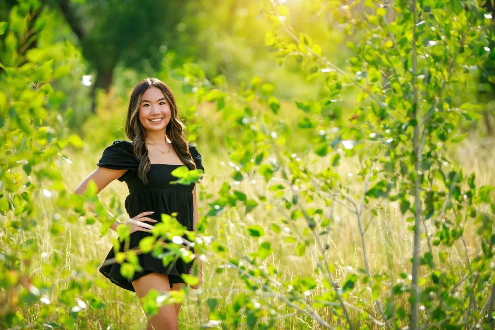 A person in a black dress poses among tall yellow wildflowers in a sunny meadow on a bright summer day.