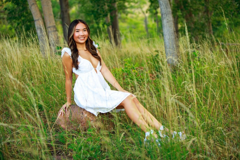Outdoor portrait sitting on a log in a grassy field wearing a white sundress.