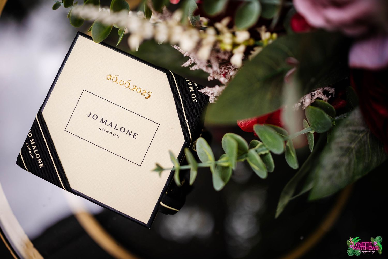Jo Malone luxury perfume box displayed among green eucalyptus leaves and floral arrangements in soft lighting at Bartle Hall