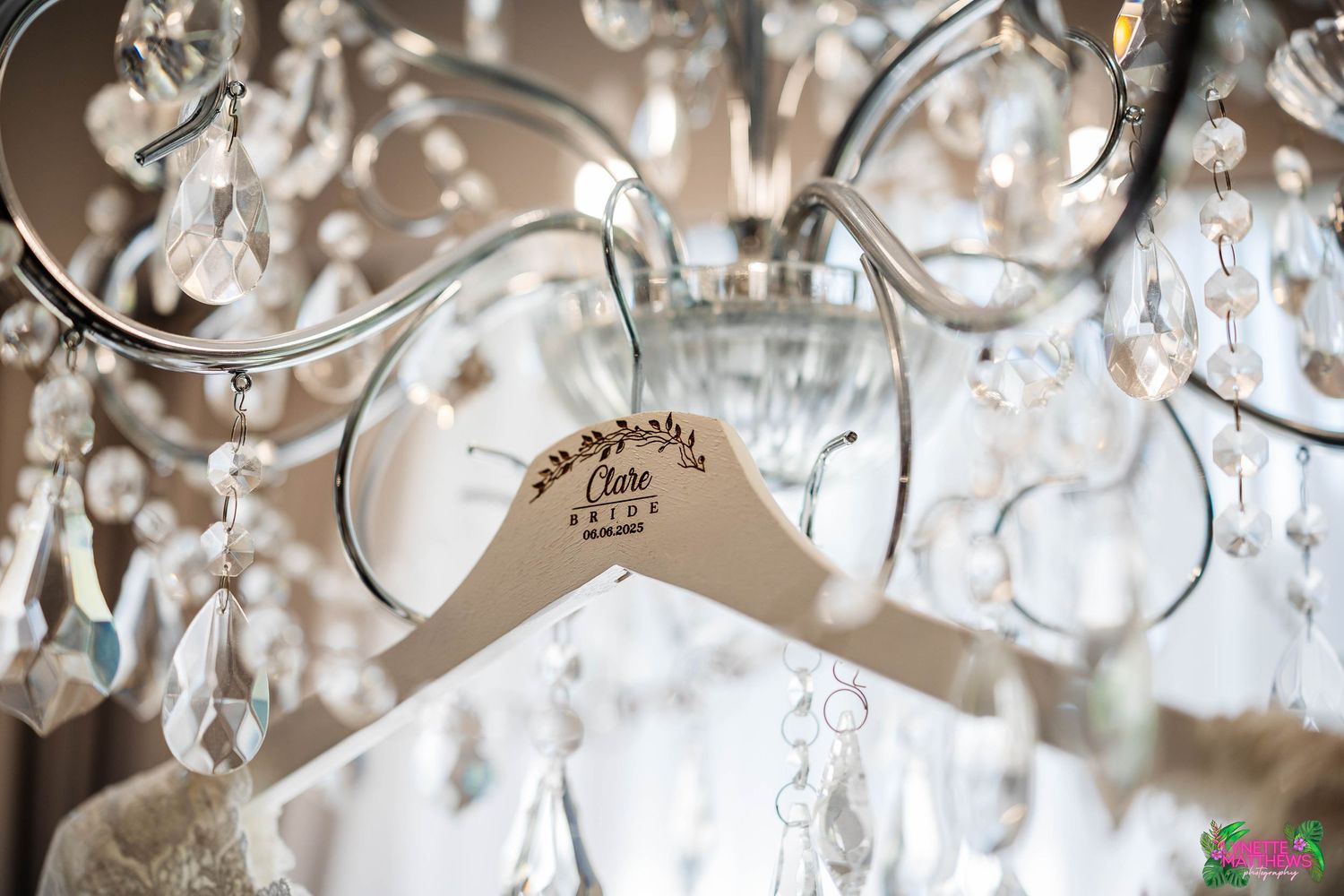 A personalised wedding dress hanger displayed on an elegant crystal chandelier with sparkling glass details at Bartle Hall