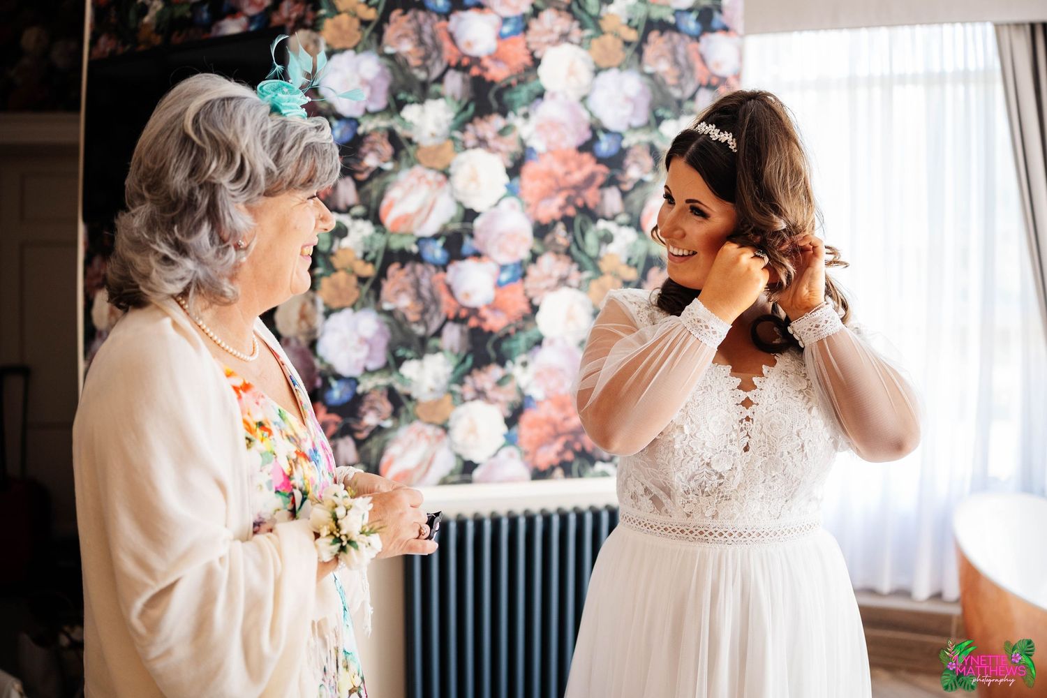 a bride and her mum share an intimate moment during wedding preparations in front of a floral backdrop at Bartle Hall