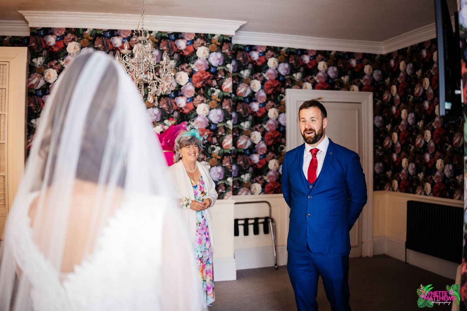 A bride and her brother share their first look moment against a floral wallpaper backdrop in an indoor setting at bartle hall