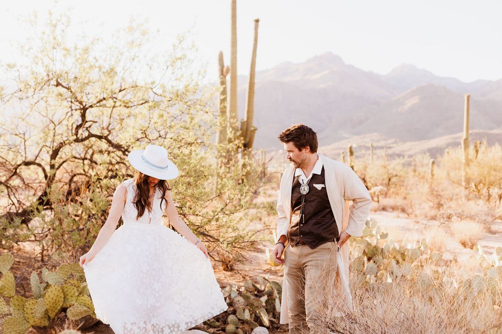 Two people celebrating their wedding surrounded by desert cacti and mountains in warm golden sunlight.