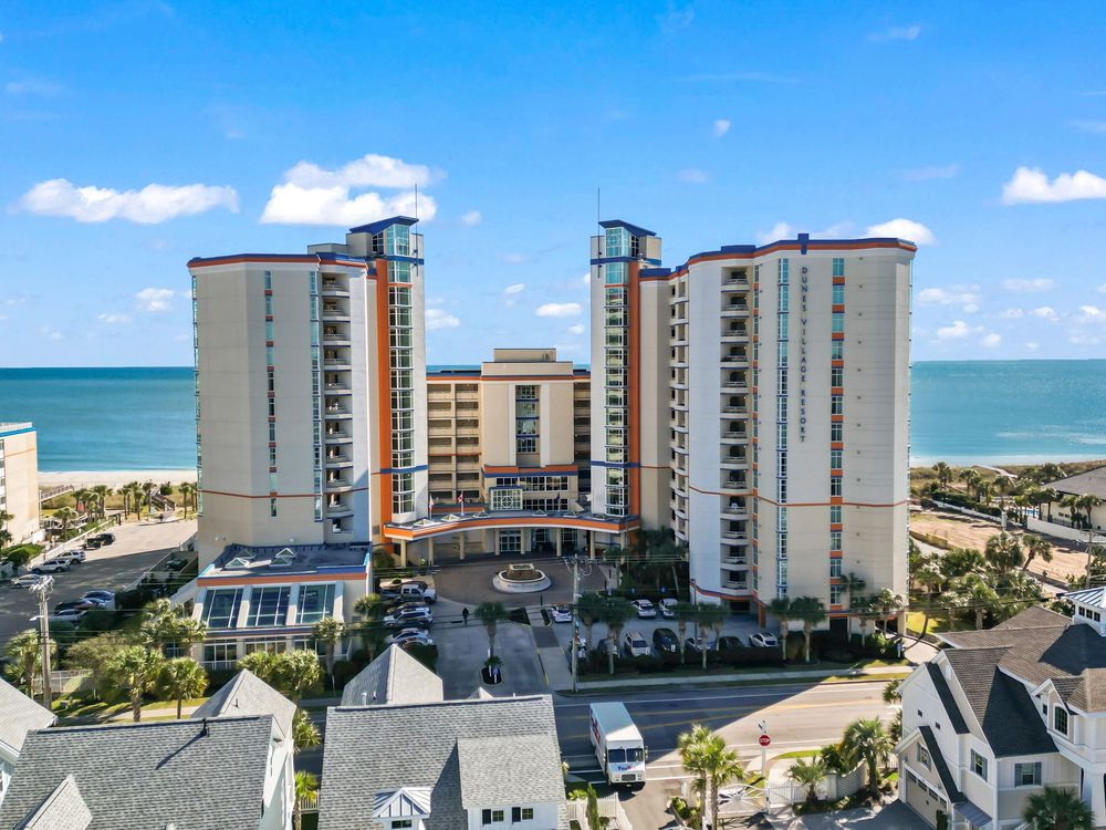 Aerial view of a beachfront high-rise resort with twin towers overlooking the ocean and surrounding area.