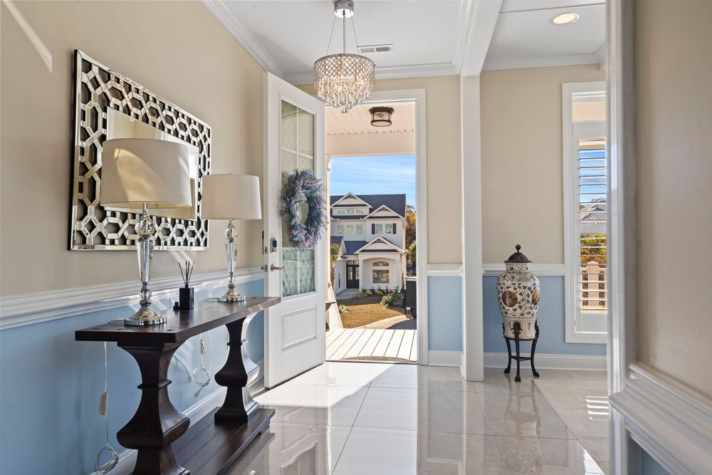 Elegant home entryway with wainscoting, chandelier, console table, and view through open front door.