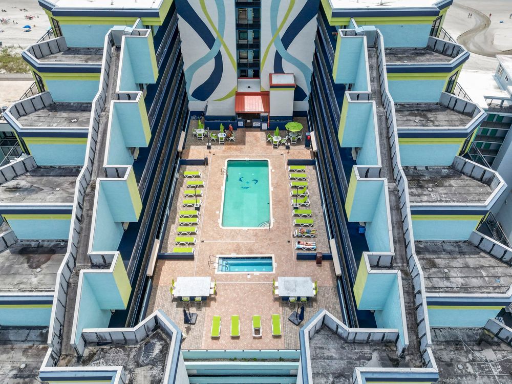Aerial view of a colorful hotel courtyard featuring a rectangular pool surrounded by lounge chairs.