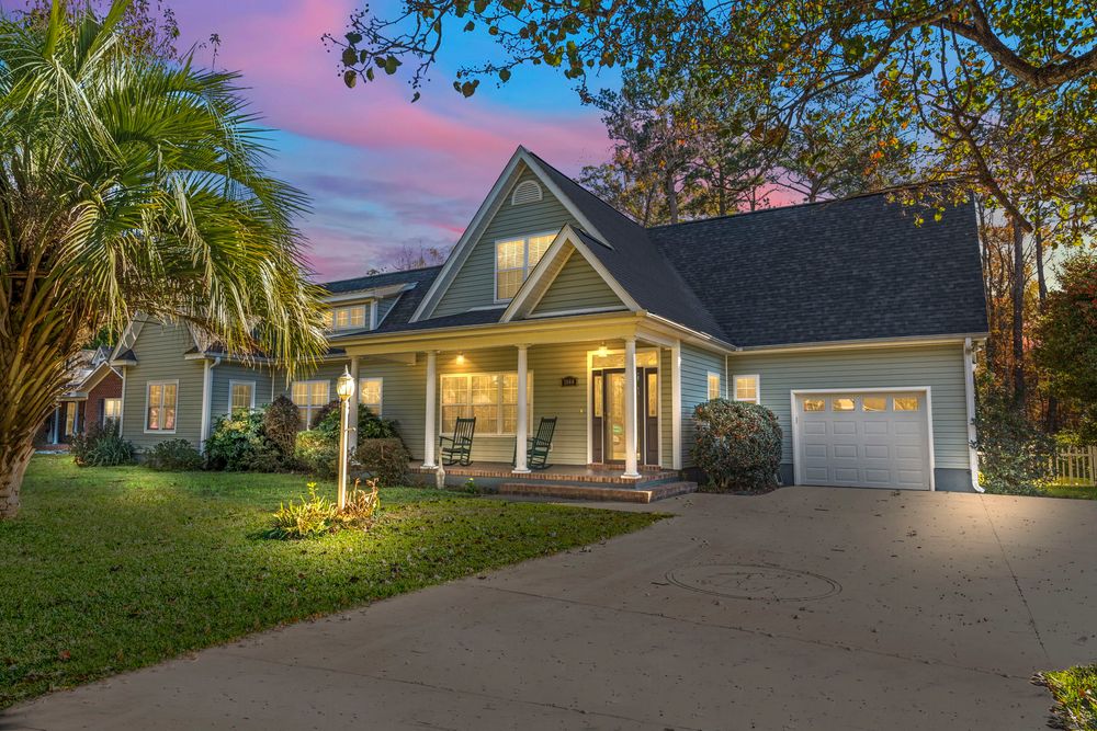 Charming craftsman-style home with covered porch, two-car garage, lush lawn, and palm trees at twilight.