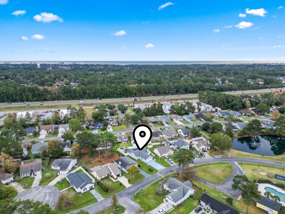 Aerial view of a suburban neighborhood with tree-lined streets, pond, and highway in the background.