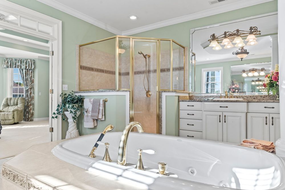 Luxurious master bathroom featuring a soaking tub, gold fixtures, glass shower, and white vanity cabinets with granite countertops.