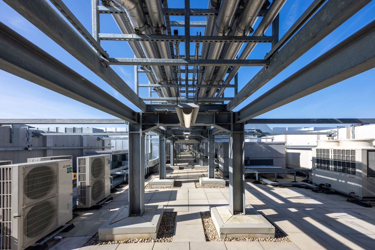 Industrial rooftop HVAC system with metal beams and air conditioning units under geometric structural framework.