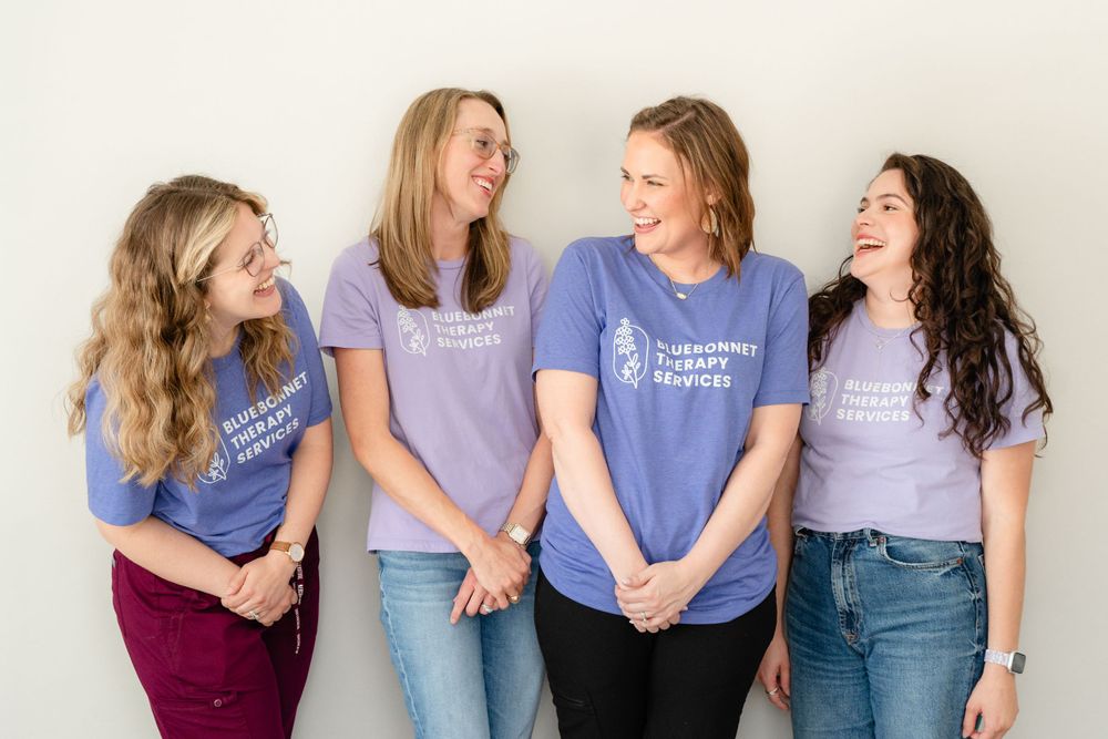 Four people wearing matching purple t-shirts laughing together against a white wall.