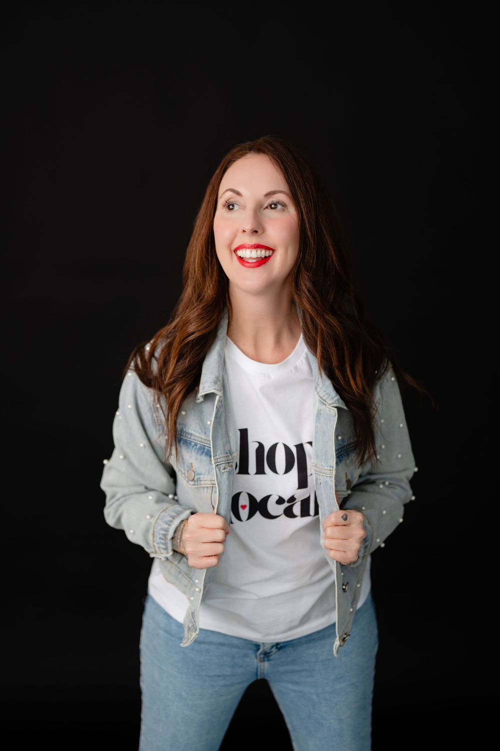 Person wearing a white graphic t-shirt and light denim jacket poses against a dark background.