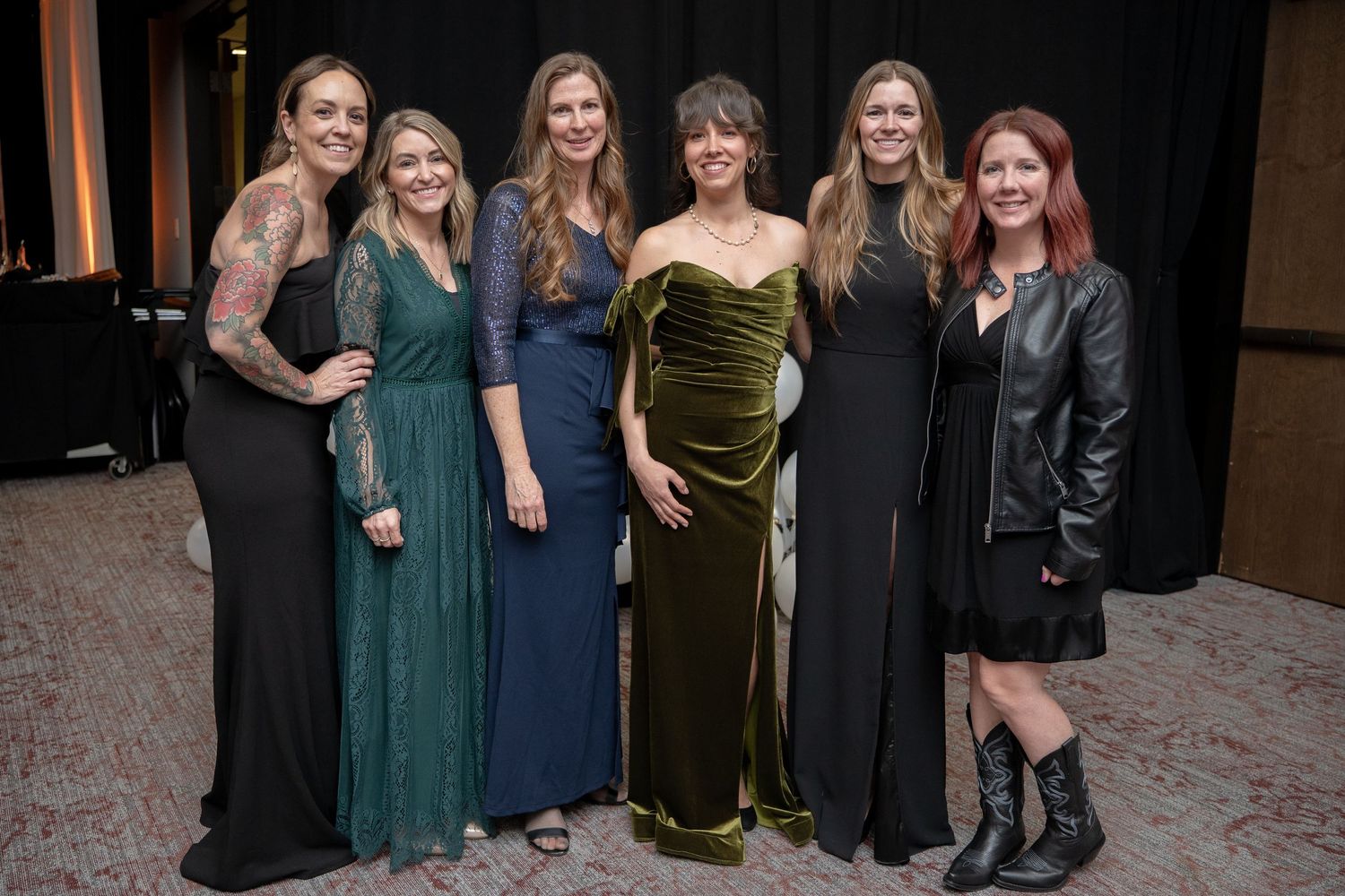 Six women in formal attire posing together at an elegant evening gala event.