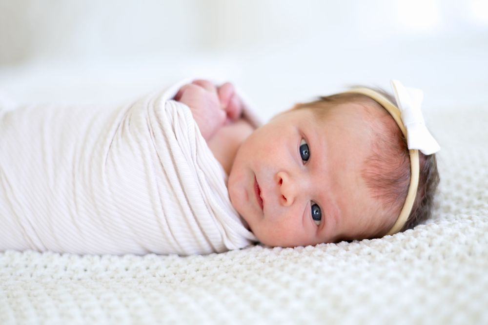 Newborn girl swaddled in white blanket looking at camera during her in-home newborn photography session in Athens, GA.