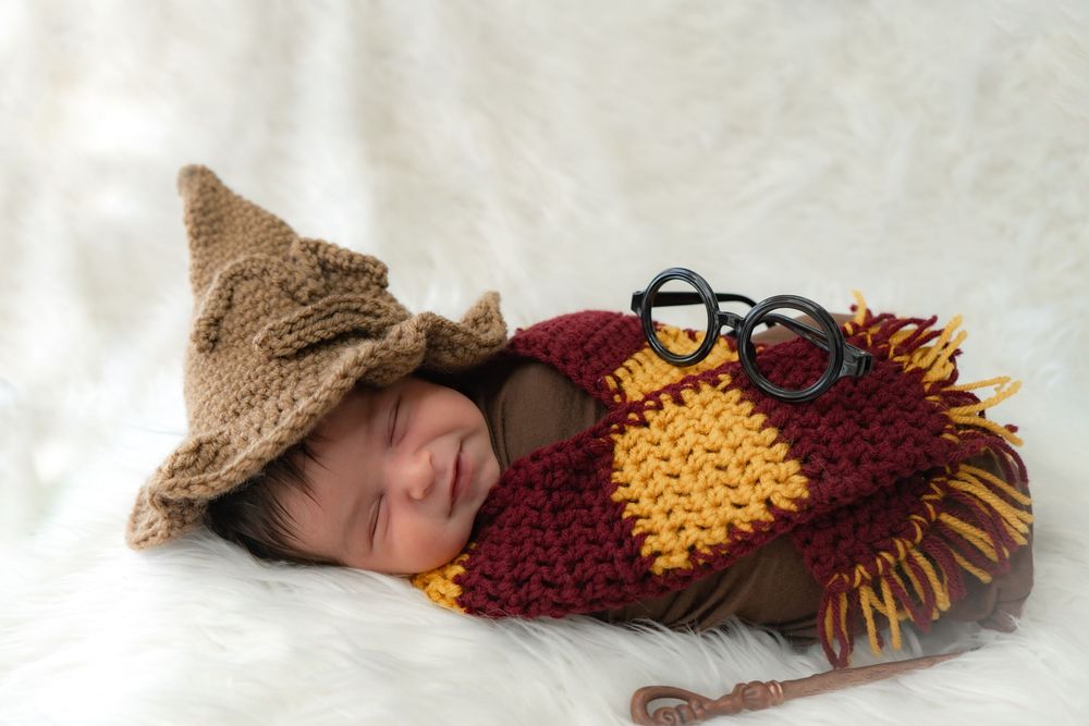 Sleeping baby wearing cozy knitted owl outfit with brown hat and glasses rests on soft white blanket.