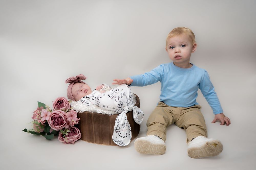 A young child lays on a white floor with pink flowers wearing a light blue sweater and khaki pants.