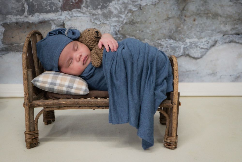 Sleeping baby on rustic wooden bench with plaid pillow and blue blanket.