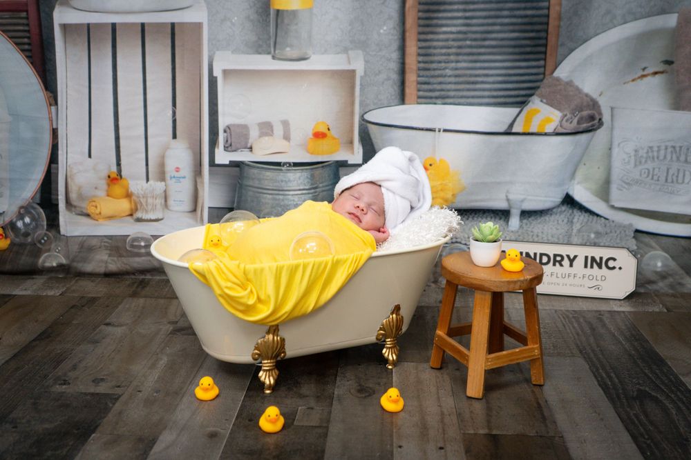 Newborn photo setup with vintage clawfoot bathtub and rubber ducks.