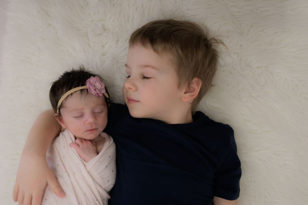 A young child in blue snuggles next to a sleeping baby wrapped in pink and white.