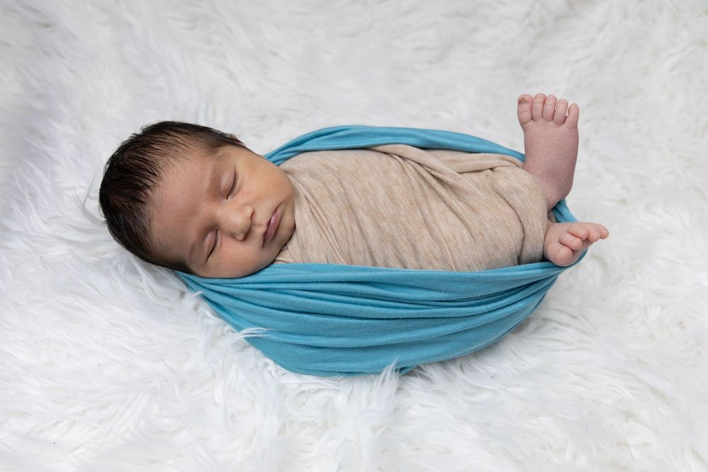 Peacefully sleeping infant wrapped in soft turquoise fabric lying on white fluffy background.