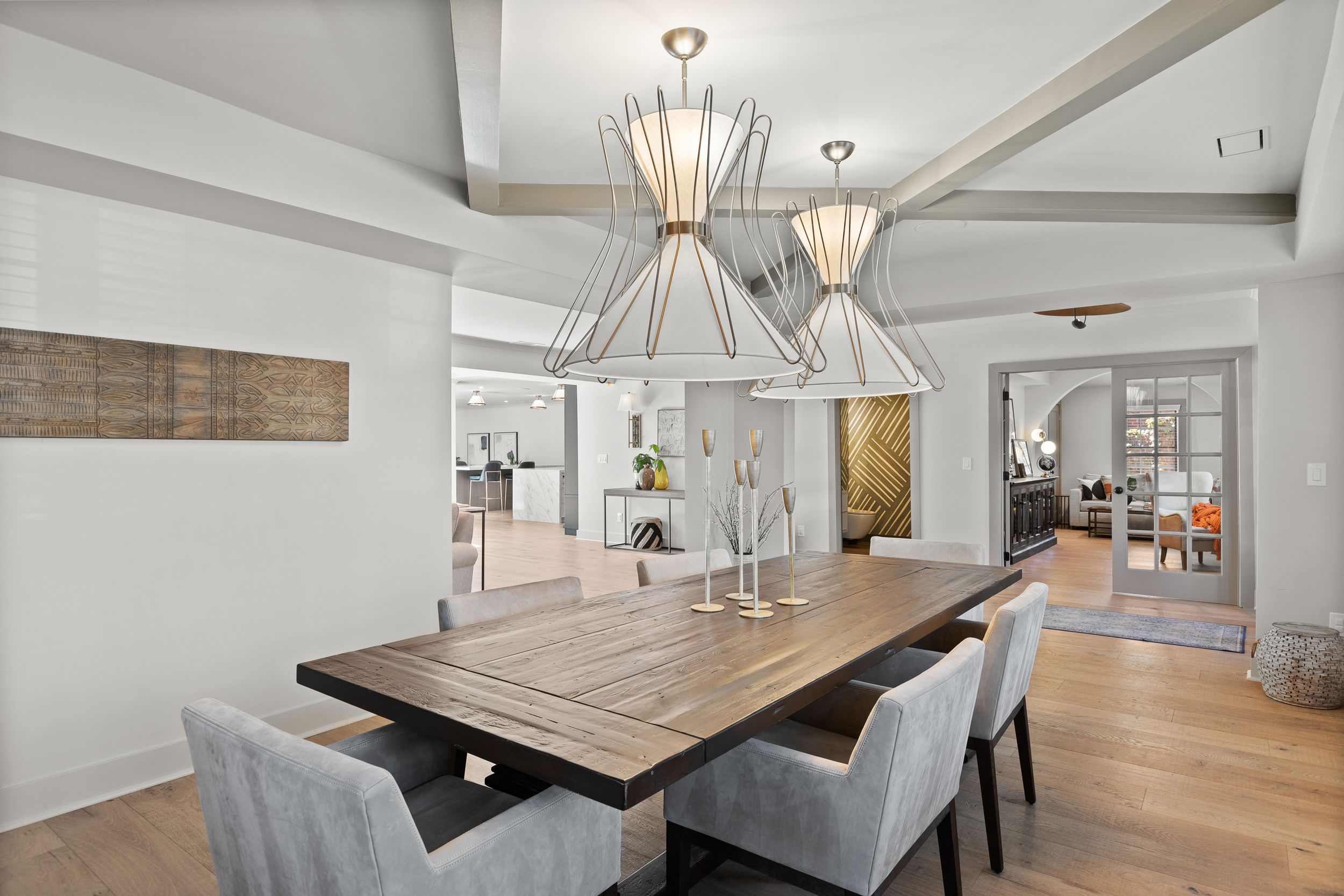 Modern dining room featuring a rustic wooden table, grey upholstered chairs and two elegant chrome pendant lights. Real estate photography.