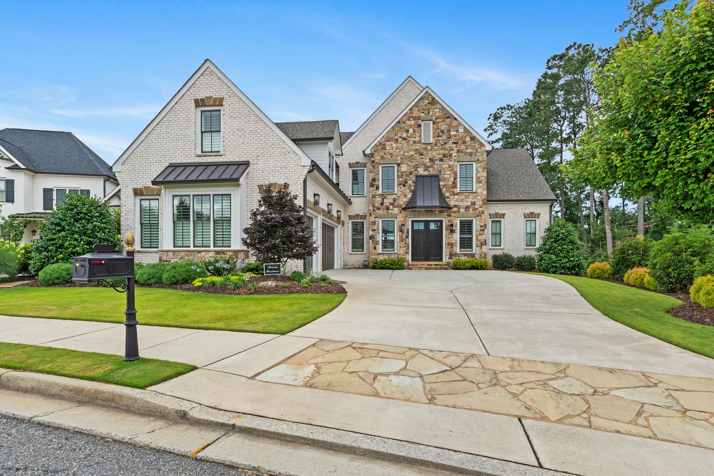 Luxurious stone mansion with curved driveway and manicured landscaping in an upscale neighborhood. Real estate photography.