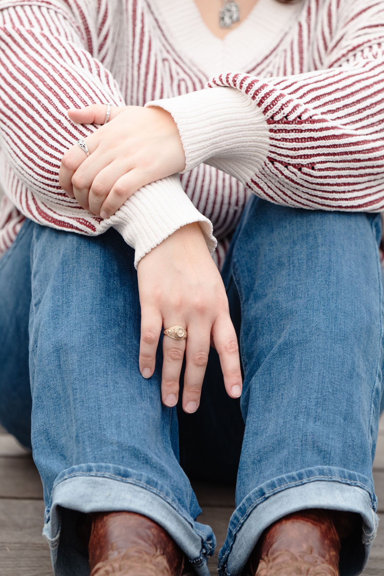 Close-up view of someone wearing a striped sweater and cuffed jeans with brown boots, displaying a ring on their hand.
