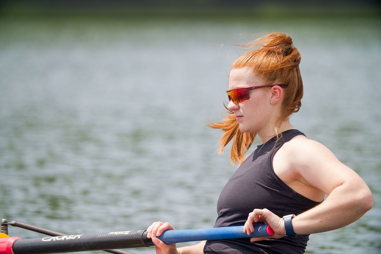 Rower in dark activewear and sunglasses training on the water during a sunny day.