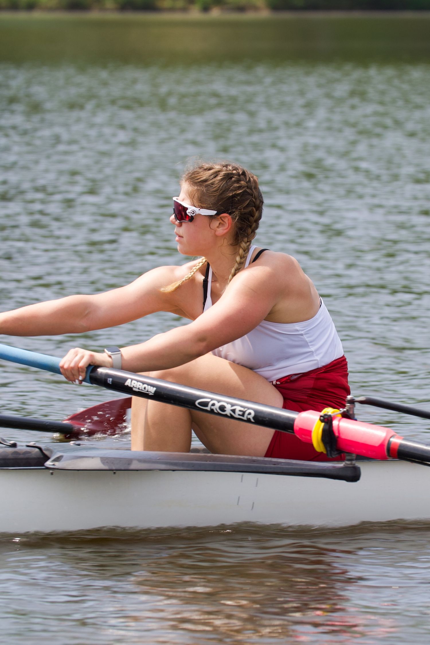 Close-up of rower in white tank top and red shorts using Croker oars during training session.