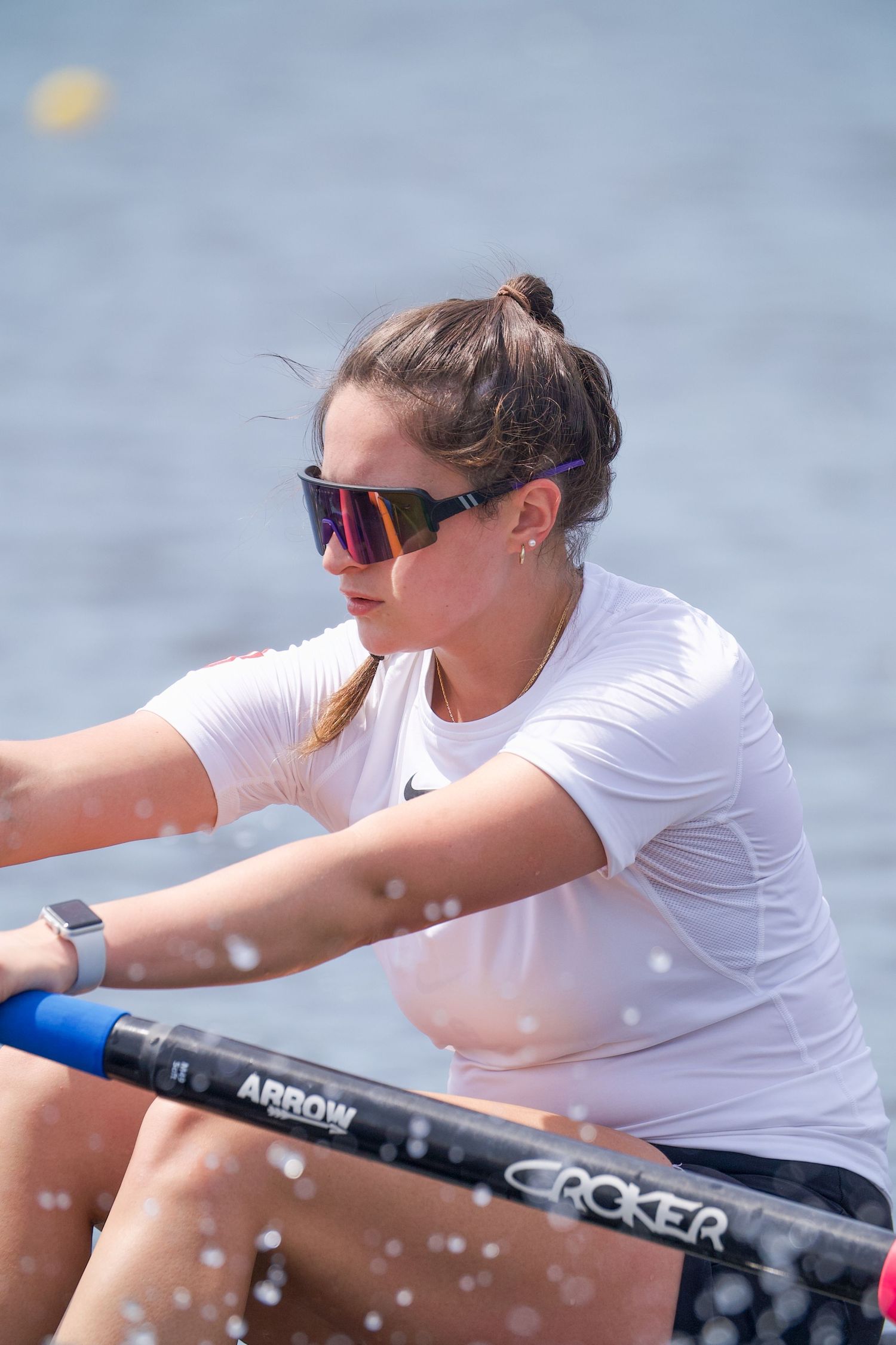 Rowing team members in white uniforms practice synchronized rowing techniques on tranquil waters.