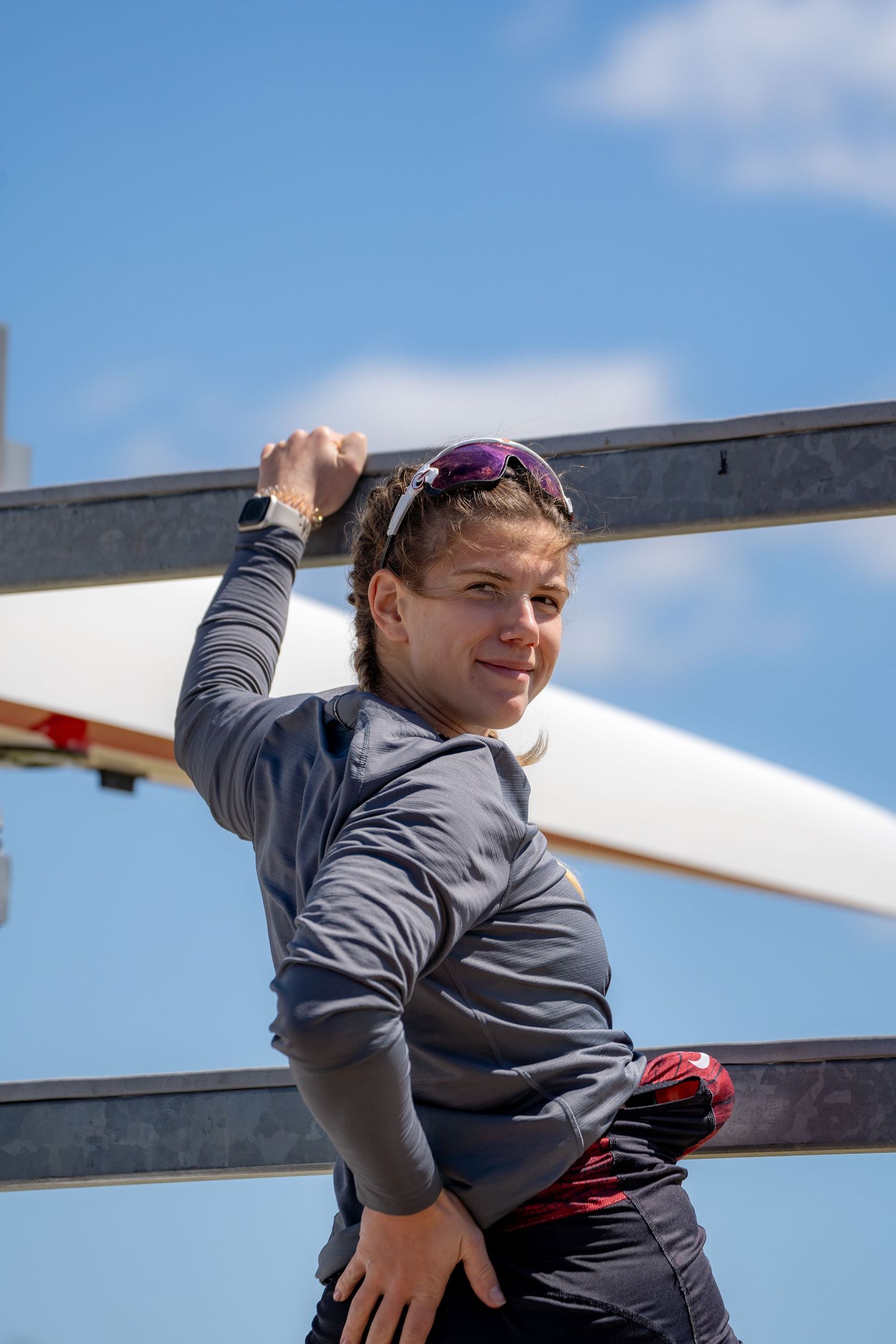 A person in athletic wear exercises on outdoor fitness equipment against a blue sky with white clouds.