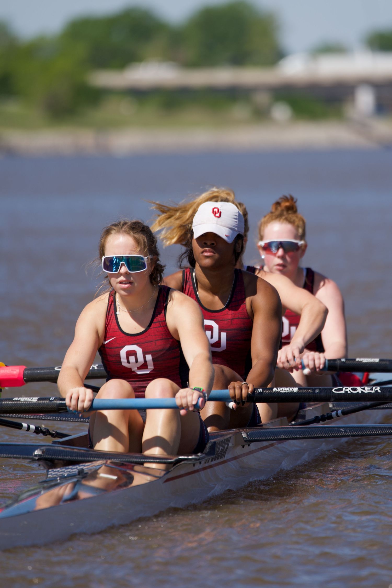 Collegiate rowing team in crimson uniforms gliding across water during competitive racing practice.