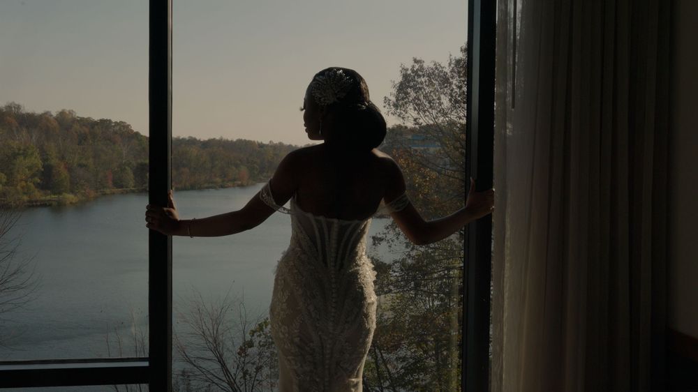 People standing silhouetted against large windows overlooking a scenic lake view at sunset.