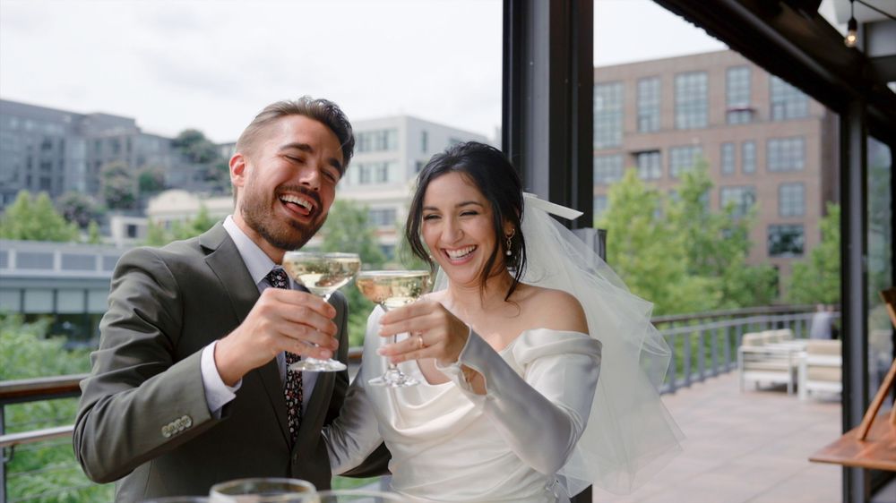 A happy couple toasts with champagne glasses at an elegant outdoor restaurant terrace during their wedding celebration.