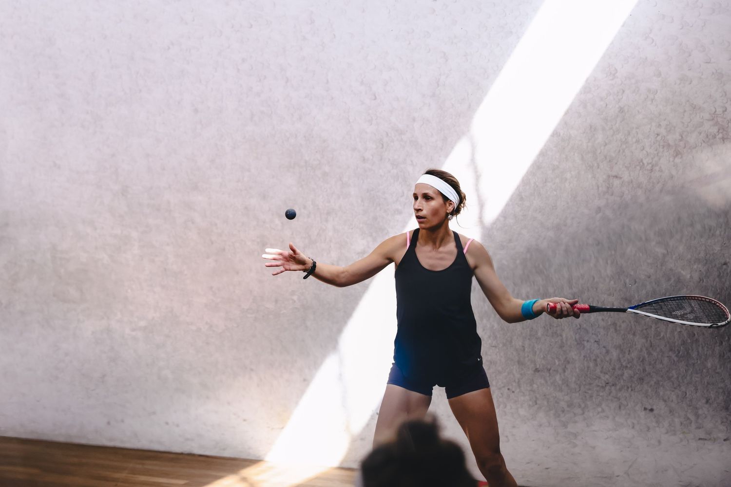 An athlete competes in a fast-paced squash match on a wooden court, chasing the ball during gameplay.