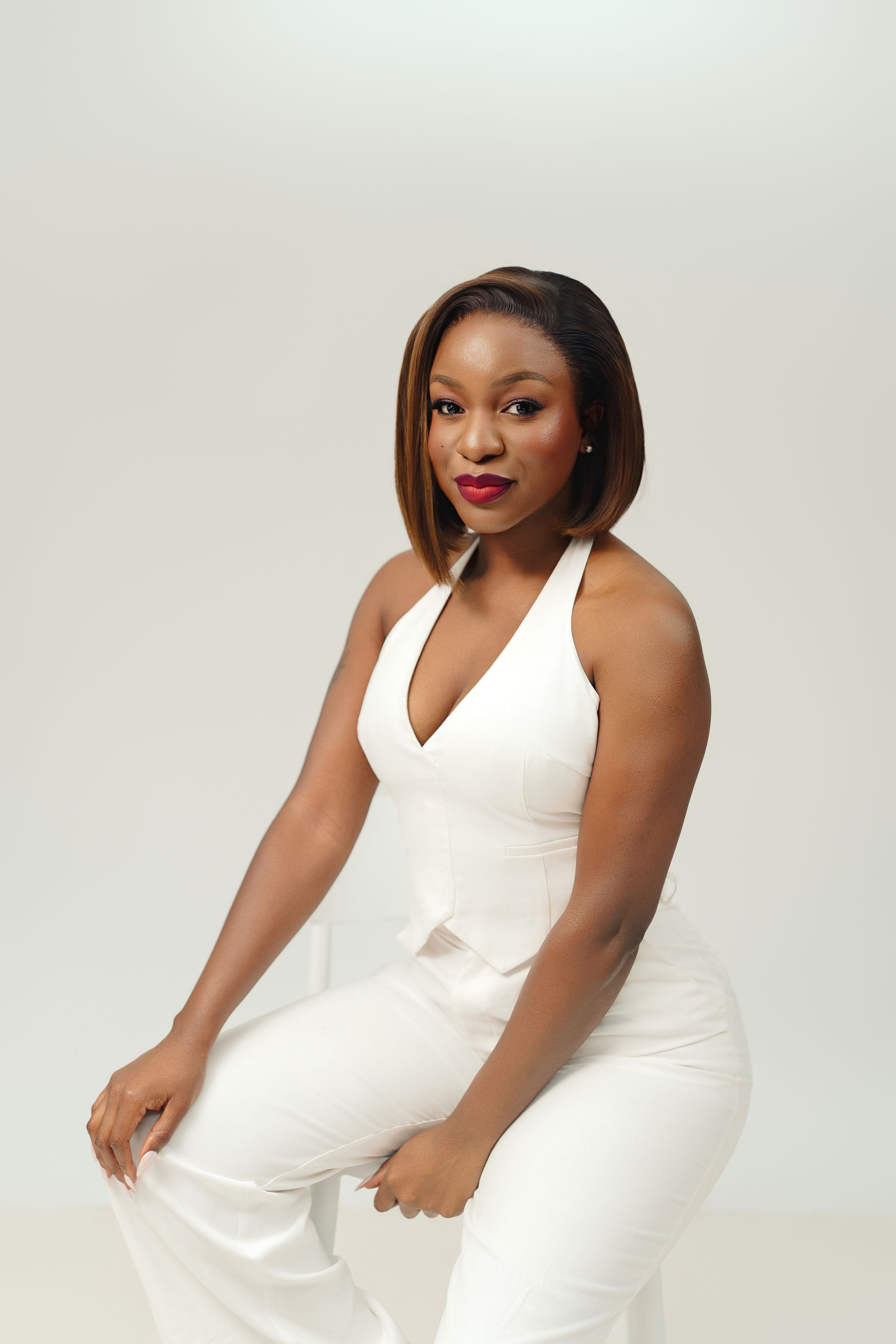 Professional studio portrait of a confident woman in an elegant white halter jumpsuit posing against a light gray backdrop.