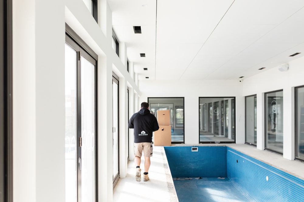 Modern indoor swimming pool with large windows and white corridor in residential building.