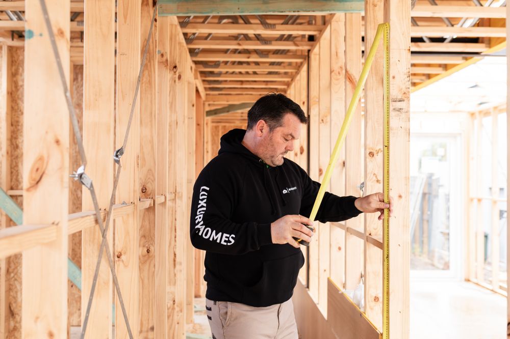 Workers reviewing construction plans inside framed residential building structure.