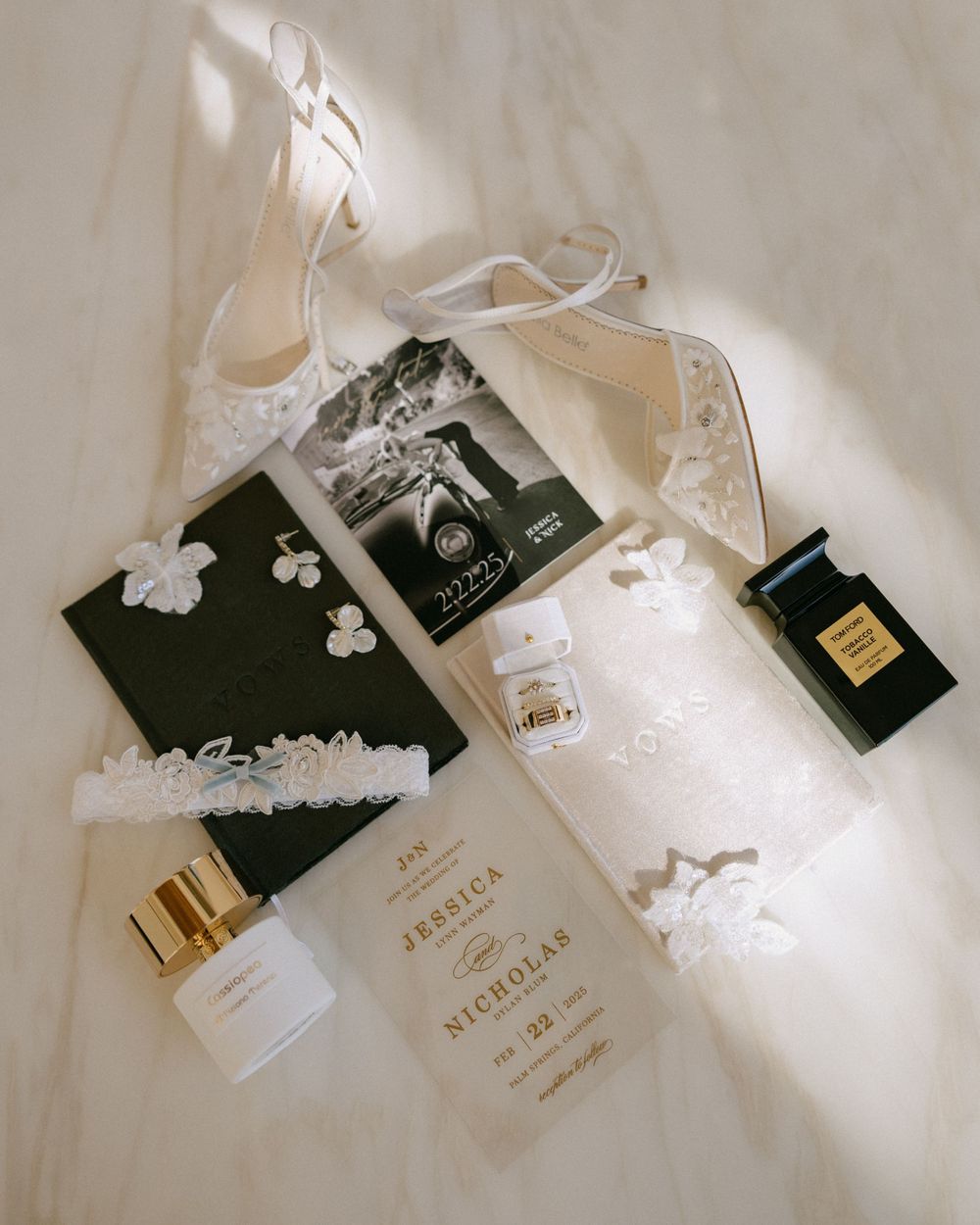 Flat lay of bridal accessories including lace heels, perfume, garter, and wedding stationery.