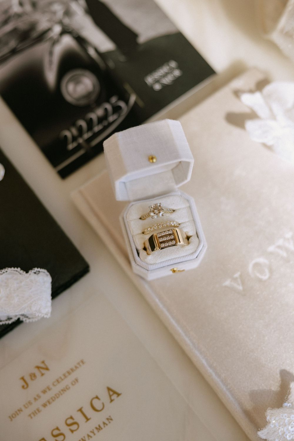 Gold wedding rings displayed in white velvet ring box with wedding stationery and vow books.