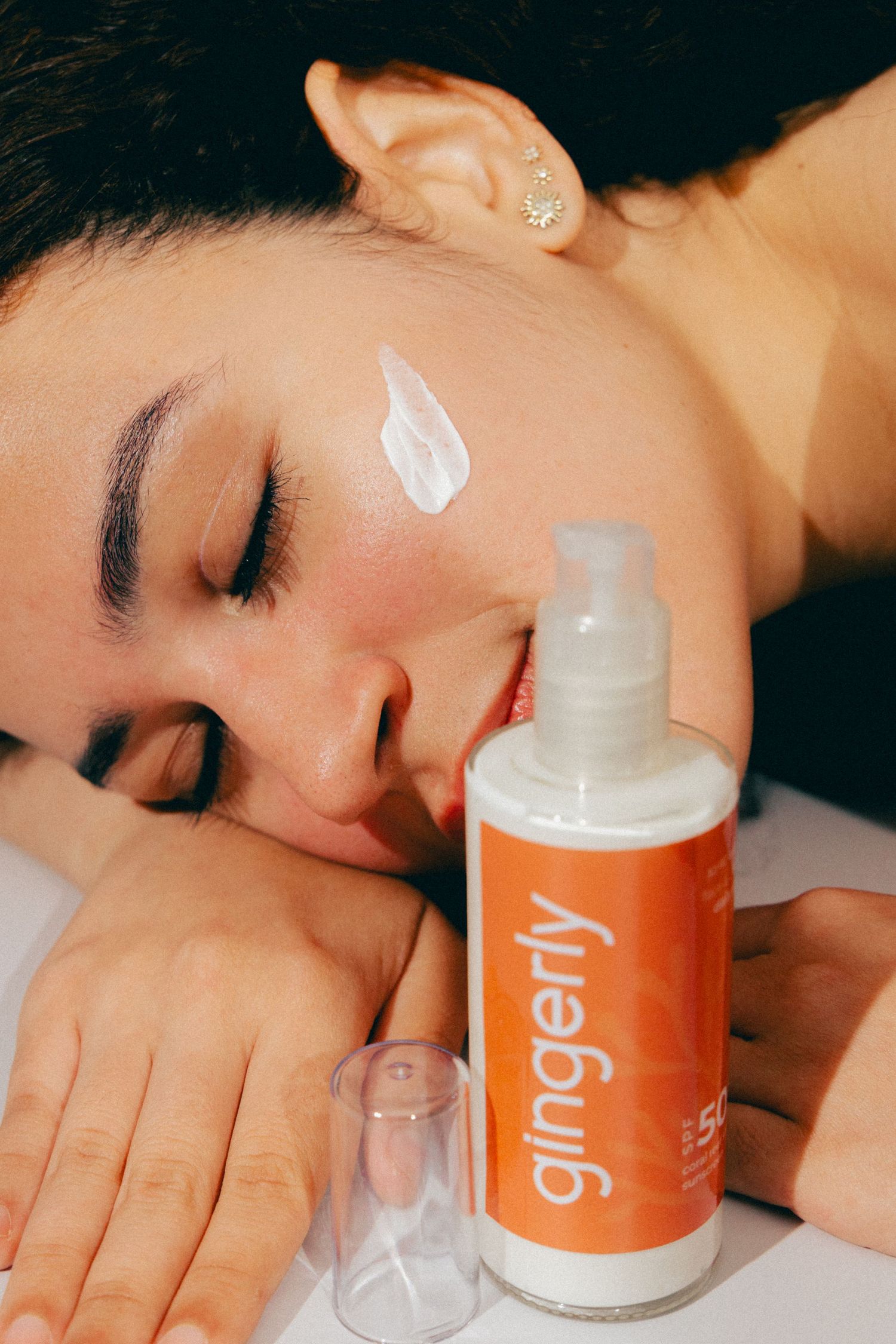 Orange Gingerly skincare product bottle with cream application on relaxed face.