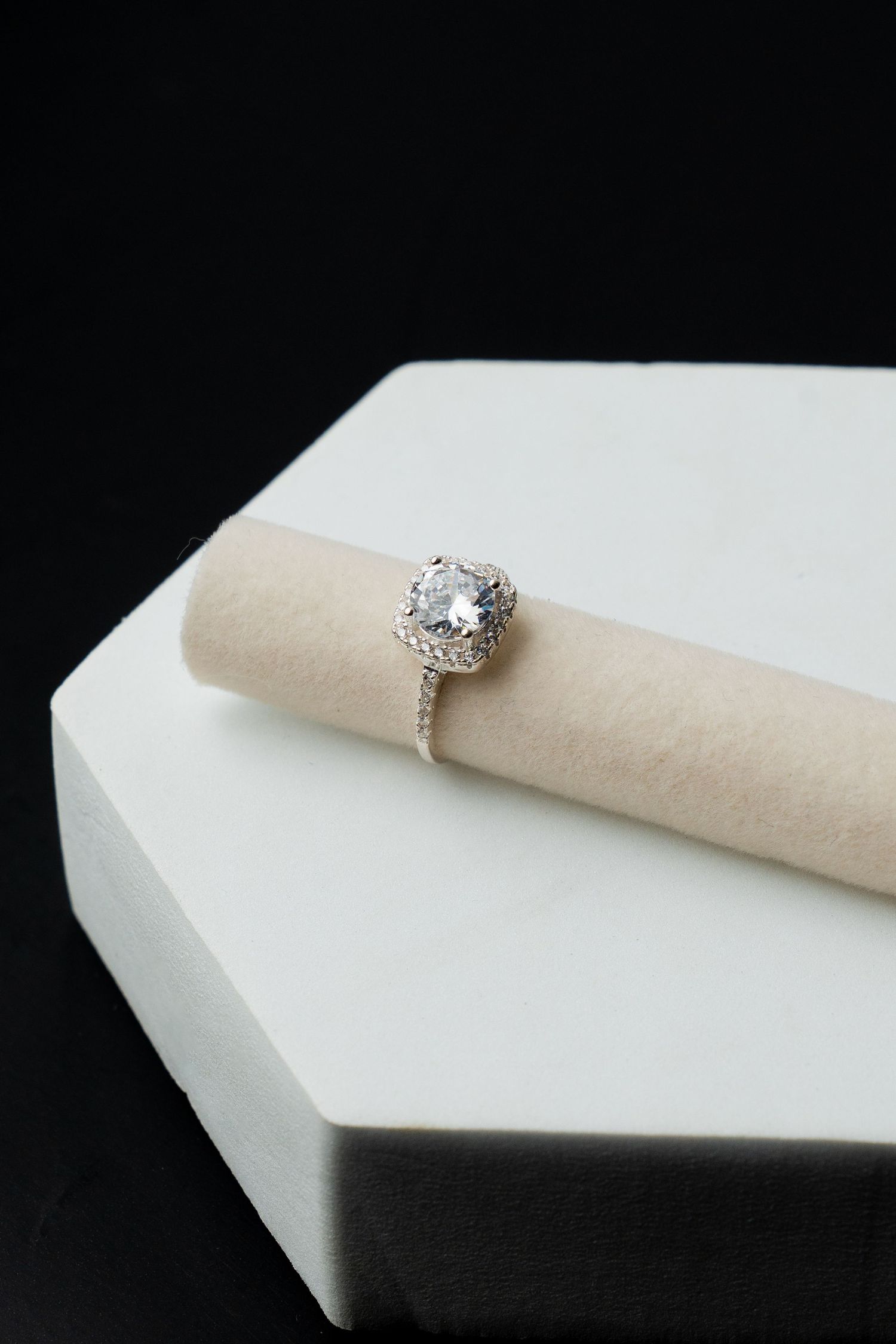 Elegant silver halo engagement ring with round diamond center stone displayed on a beige velvet ring holder.