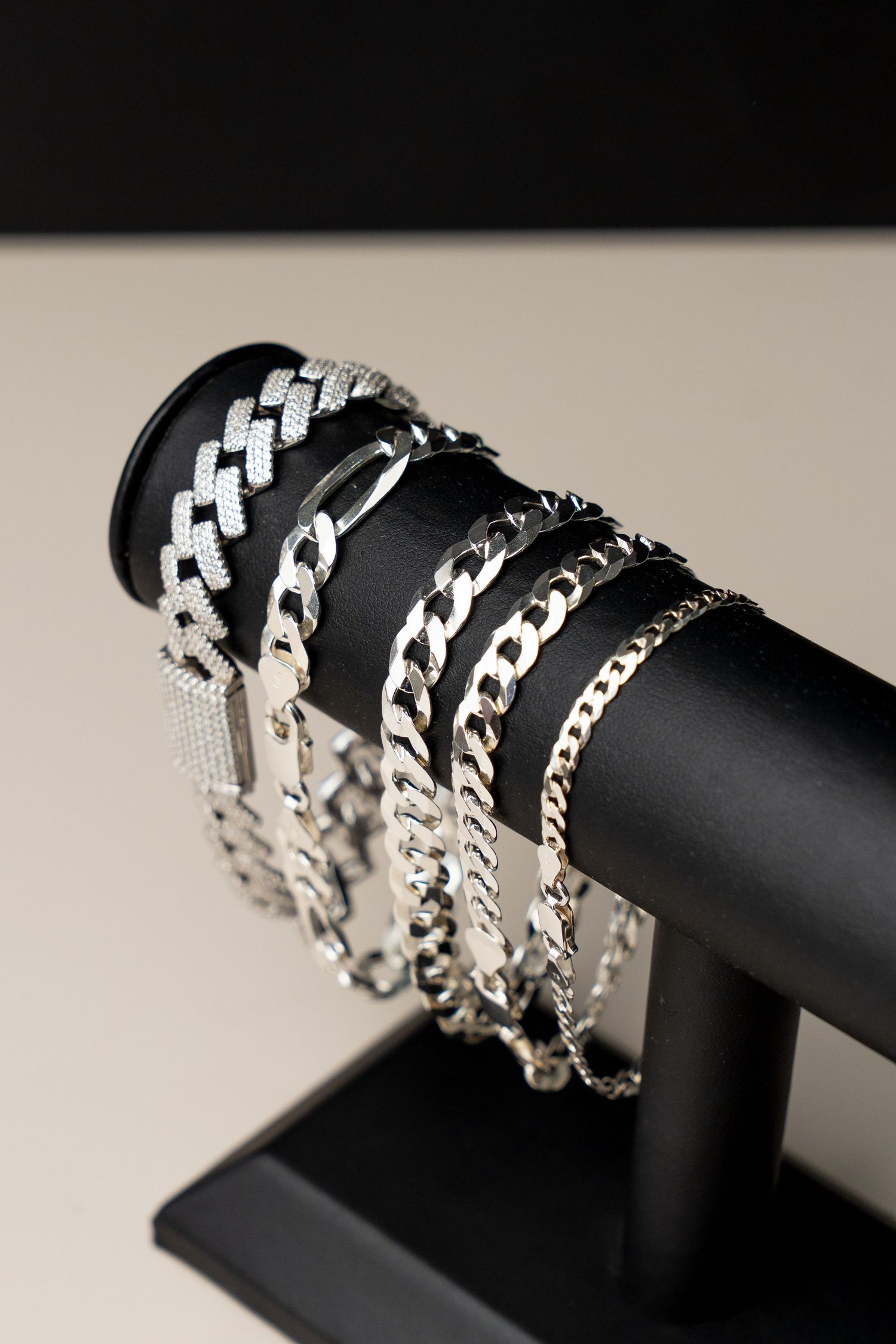 Multiple silver chain bracelets displayed on a black jewelry stand, featuring various link styles and sizes.