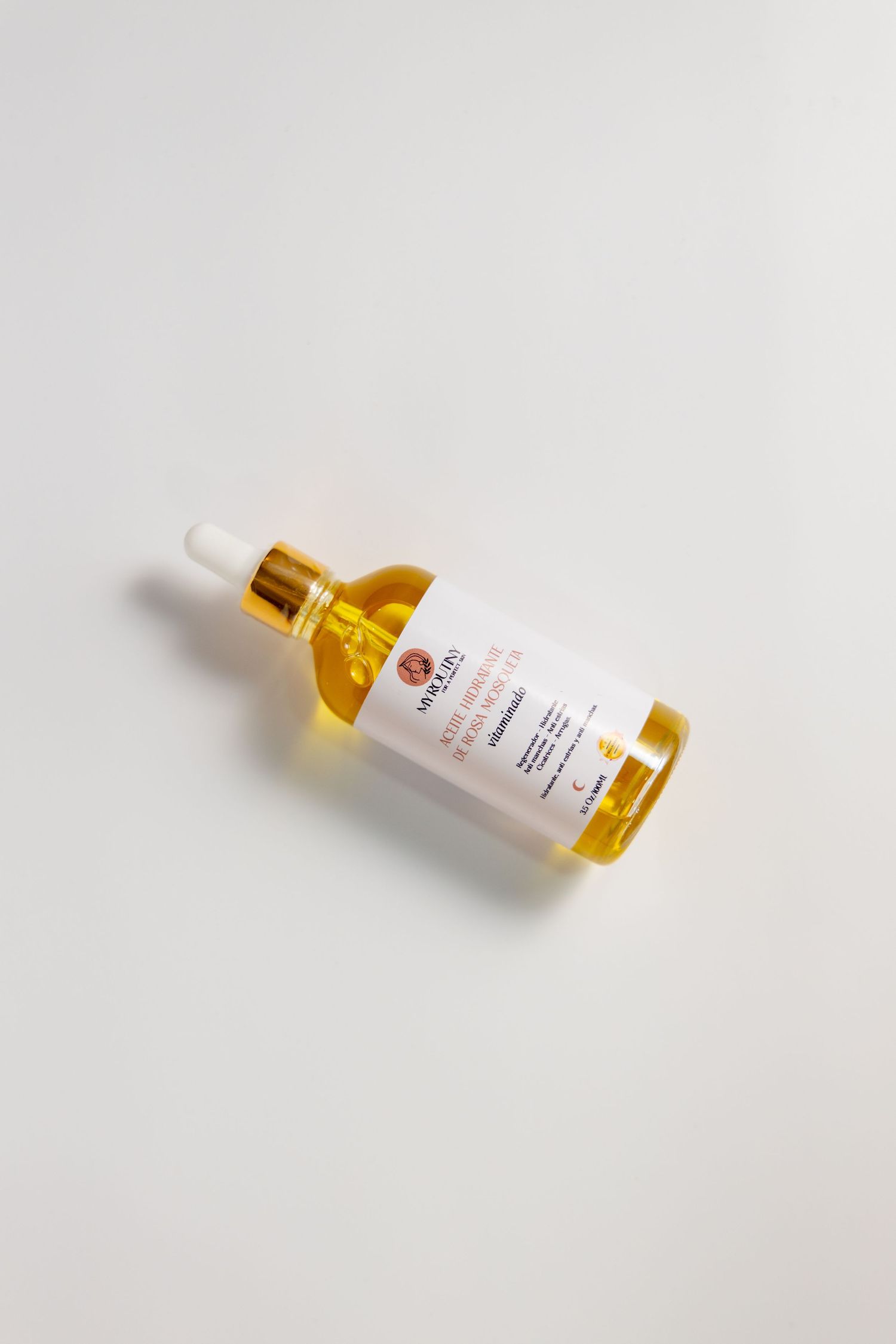 A glass bottle of golden skincare oil with dropper against white background.