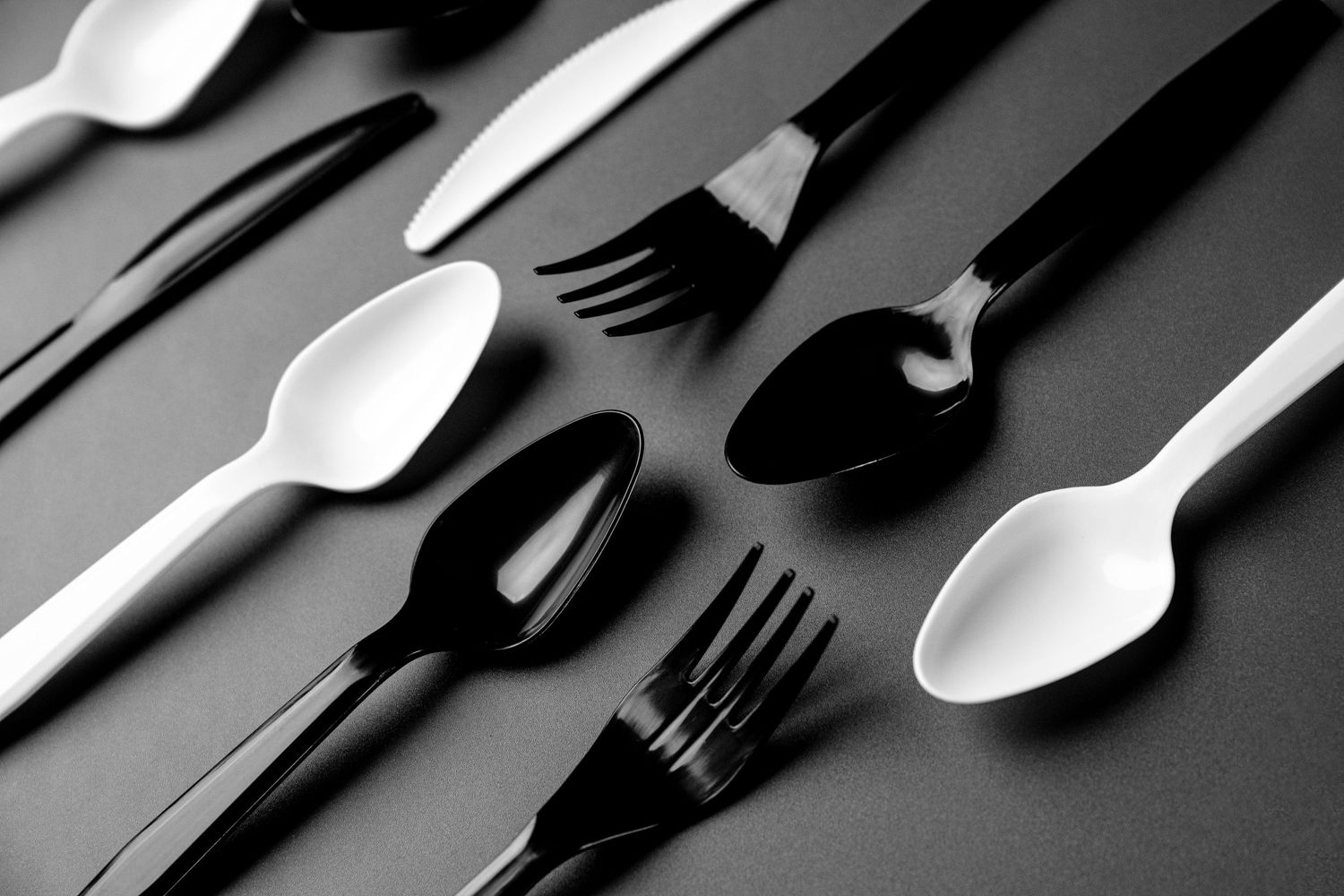 Black and white flatware arranged in alternating pattern on dark background.