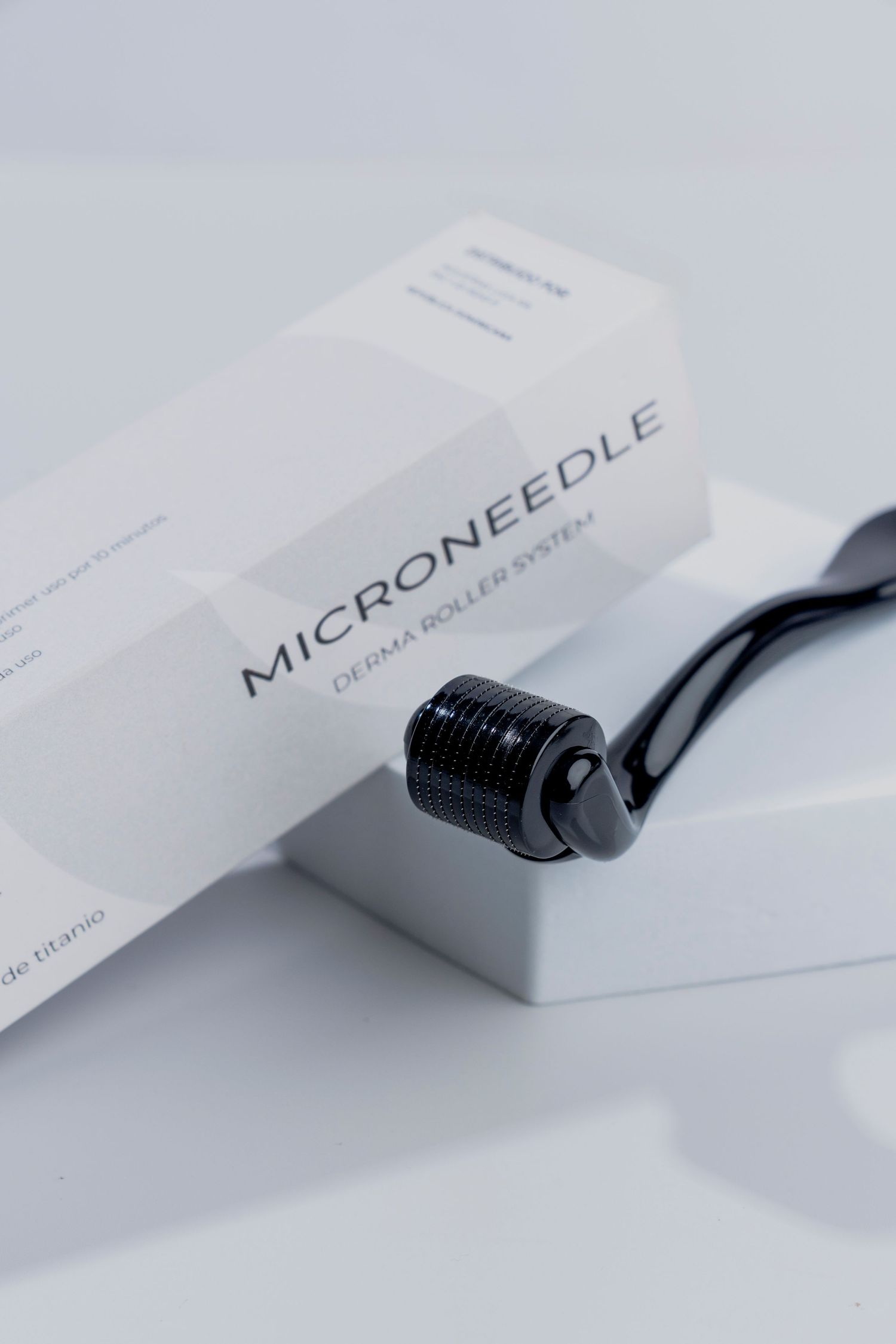 Black microneedle roller device next to its white packaging box.