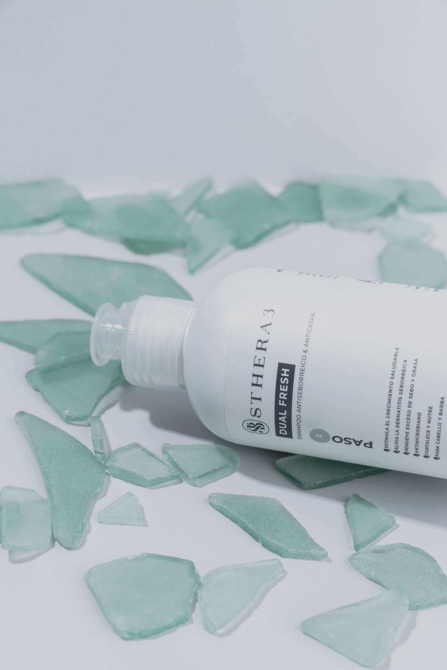 White cosmetic bottle surrounded by scattered sea glass pieces on white background.
