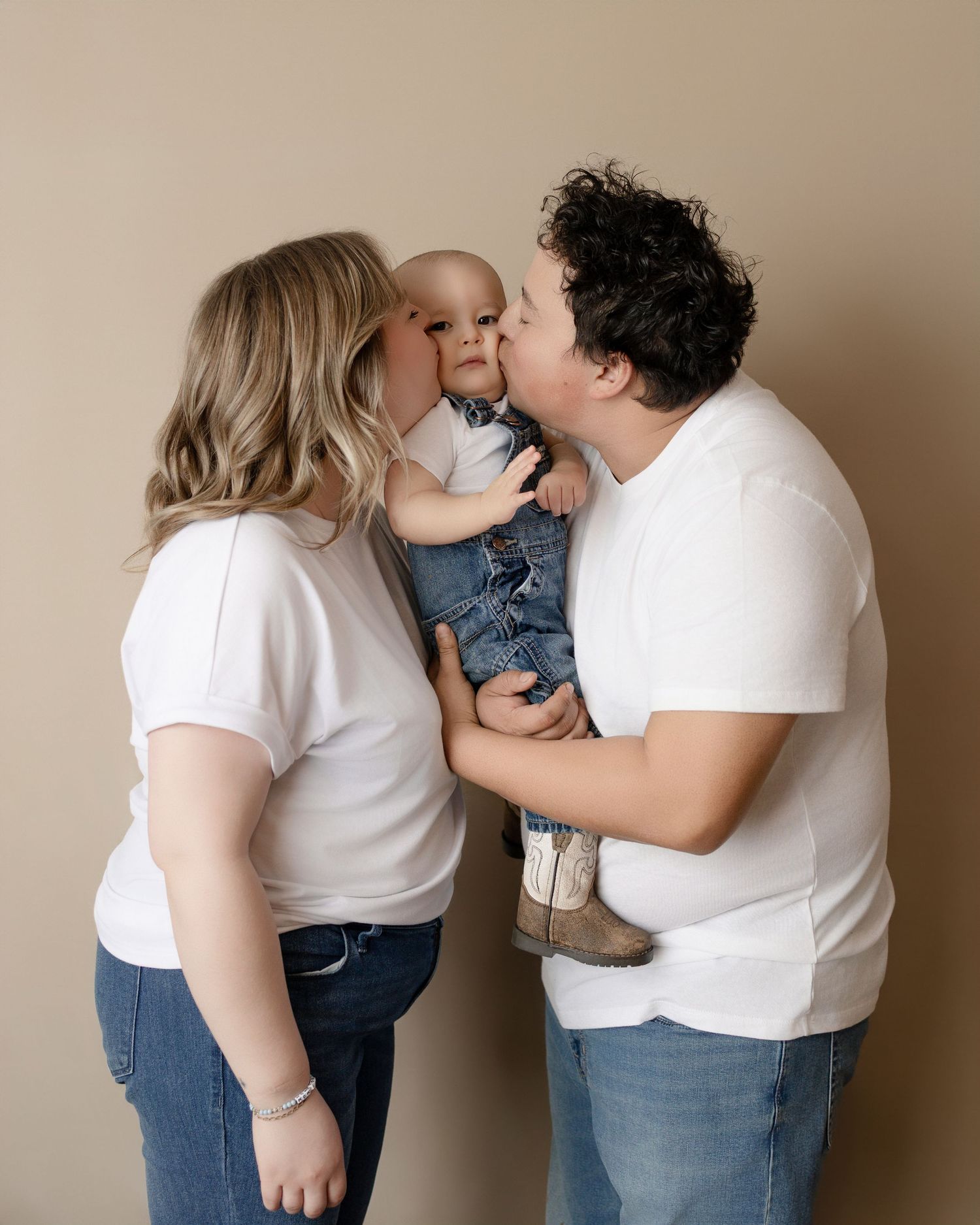 A family shares an intimate moment wearing matching white shirts and jeans against a neutral backdrop.