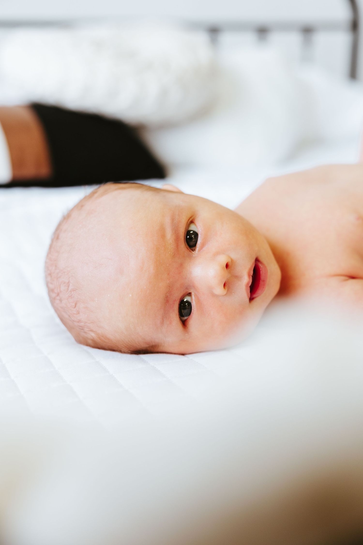 Baby lying on white bedding looking at the camera.