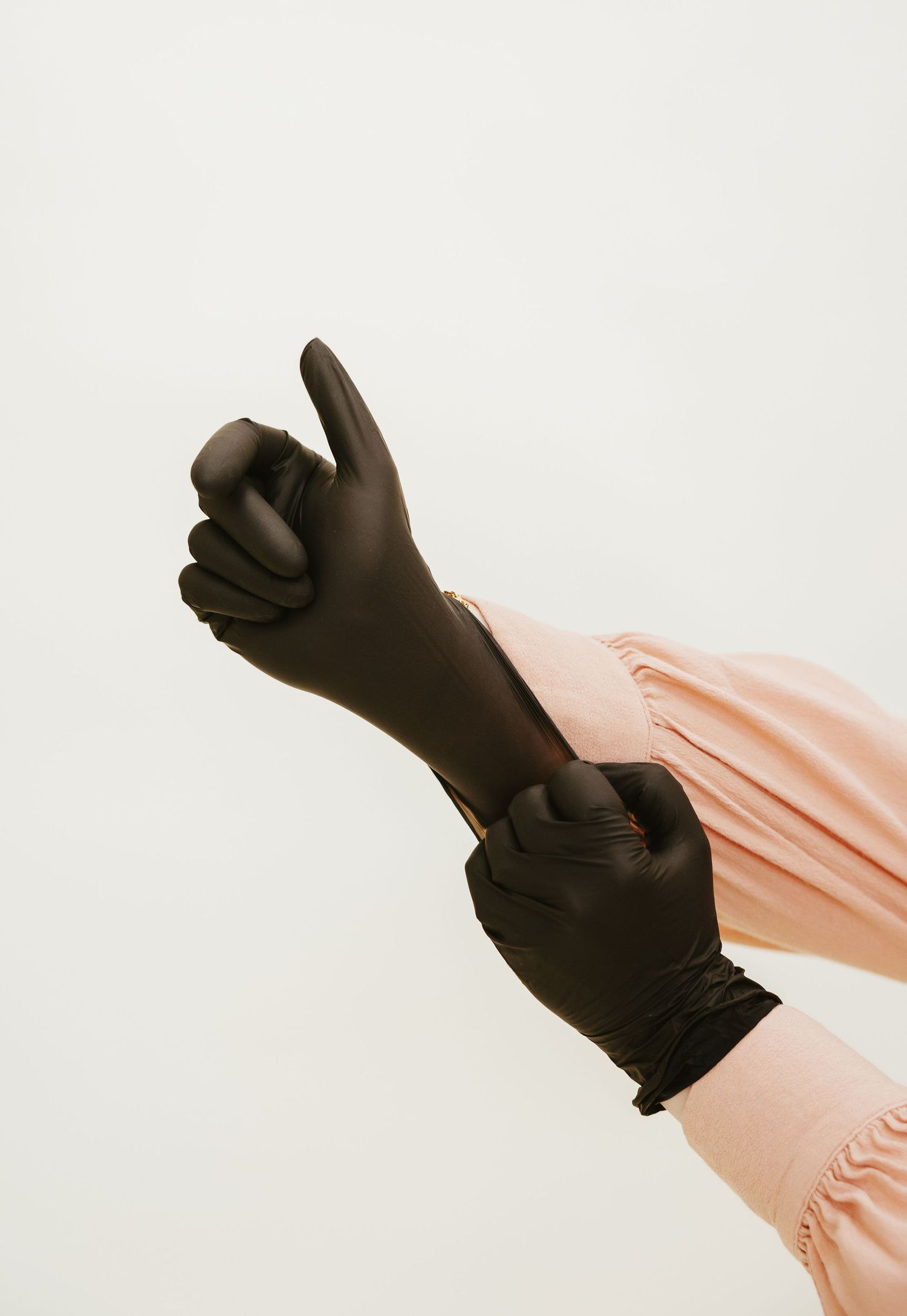 Hands wearing black protective gloves making a thumbs up gesture against a light background.